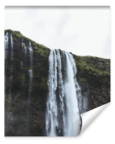 low angle view of Seljalandsfoss waterfall in highlands under cloudy sky in Iceland 