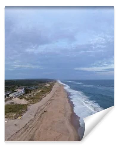 Drone panorama of Napeague on Long Islands South Fork, showing Atlantic Ocean surf, sandy beach, dunes and a beachfront resort complex at dusk.