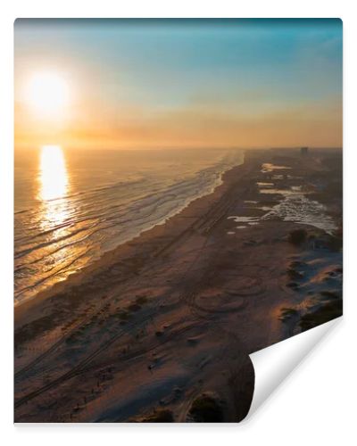 Cinematic 4K aerial drone footage captures Miramar Beach dunes at sunrise in Ciudad Madero, Tamaulipas. Warm orange and golden light paints the sky and reflects on the calm sea as the coastline stretches to the horizon. Palapas line the shore while A