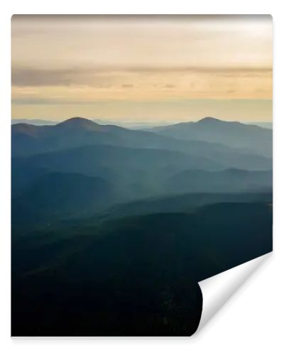 Aerial view of dark mountain hills with bright sunrays of setting sun at sunset. Hazy peaks and misty valleys in evening.