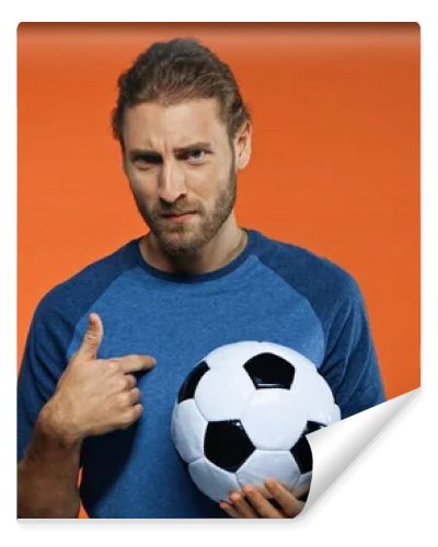 football fan in blue t-shirt holding soccer ball and pointing at himself on orange 