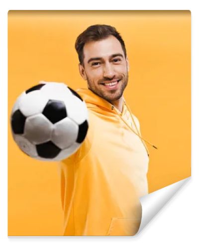 smiling man playing with football isolated on yellow