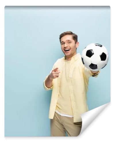 happy man in yellow shirt pointing with finger and holding football on blue