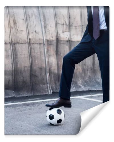 partial view of businessman in suit playing soccer on street