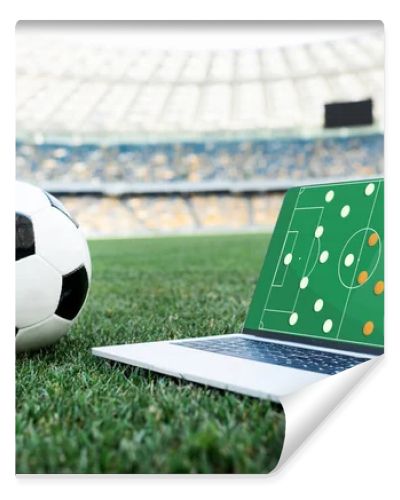 soccer ball and laptop with formation on screen on grassy football pitch at stadium