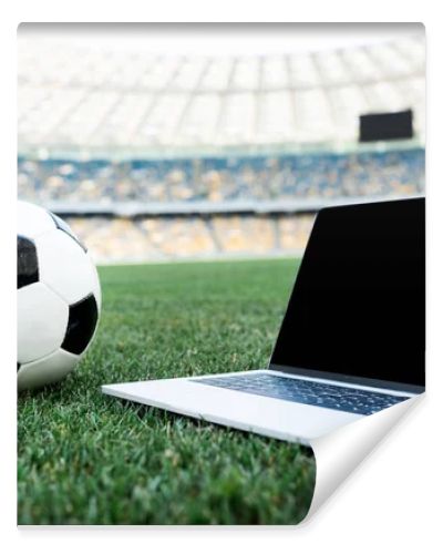 soccer ball and laptop with blank screen on grassy football pitch at stadium