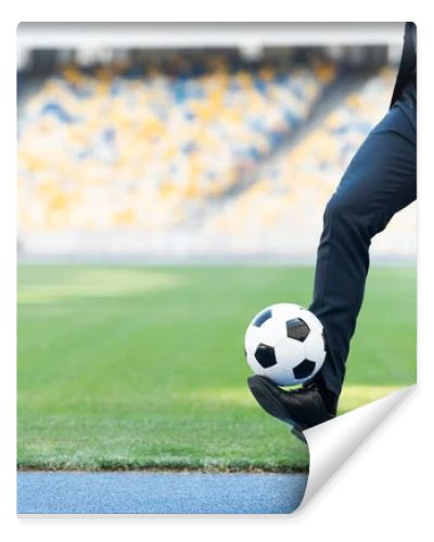 cropped view of young businessman in suit playing with soccer ball at stadium