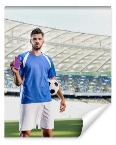 KYIV, UKRAINE - JUNE 20, 2019: professional soccer player in blue and white uniform with ball showing smartphone with Instagram app at stadium