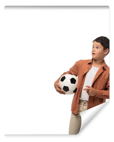 shocked boy holding soccer ball, looking away and pointing with finger isolated on white