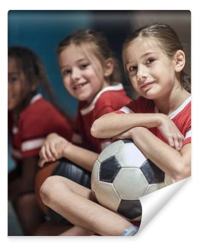 Smiling girl with soccer ball  in good mood  before training  in changing room.