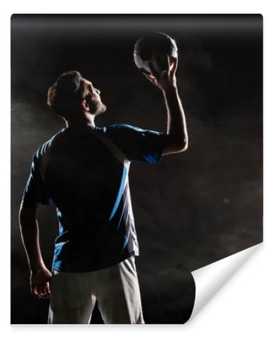 silhouette of player in uniform holding ball above head on black with smoke  