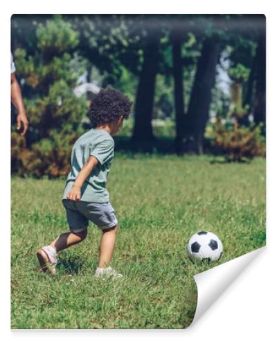 young african american father playing football with cute son in park