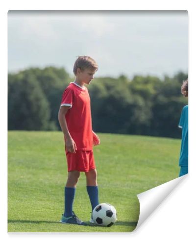 cute curly boy playing football with friend on grass in park 