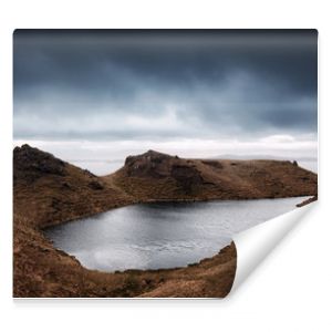 Jezioro otoczone brązowymi górami z nadciągającymi ciemnymi chmurami