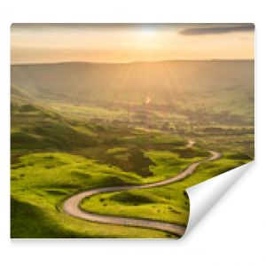 Winding country road leading to Edale in the English Peak District with beautiful golden light shining through valley.