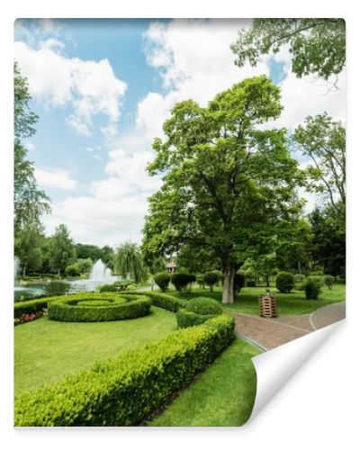 walkway near green plants, trees and fountains against blue sky 