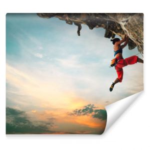Wysportowana kobieta wspinająca się na zwisającą skałę klifową na tle zachodu słońca