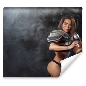 Sexy young quarterback girl with ball in smoke. American football