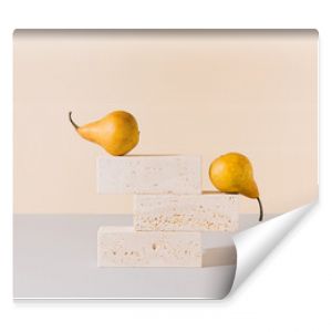 Golden yellow pears balancing on travertine marble blocks structure against gray and beige background. Creative gold summer fruit arrangement. Minimal retro styled surreal food art concept.