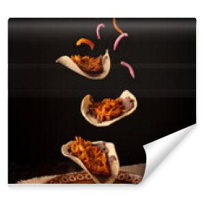 Creative food image of Mexican Tacos de Cochinita Pibil and onion with habanero chili falling on traditional mexican clay dish. Levitation photography.