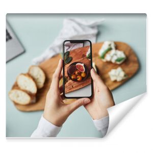 Top view of young woman taking aesthetic photo of food using smartphone in home studio, copy space