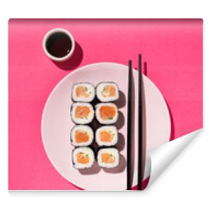 Japanese Sushi roll with salmon, cucumber and soy sauce with chopsticks in the plate on pink background with hard shadow. Concept food photography. Top view and copy space