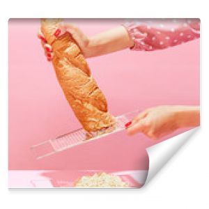 Female hands grating bread, baguette to make breadcrumb for meat isolated over pink background