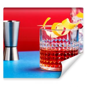 Sazerac, alcoholic cocktail drink with cognac, bourbon, absinthe, bitters, sugar and lemon zest. Dazzling red blue background with hard light and shadows pattern