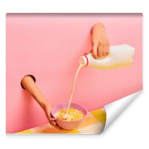 Food pop art photography. Female hands sticking out pink paper, pouring milk into bowl with corn flakes, ceral. Breakfast. Taste, creativity, art. Complementary colors. Copy space for ad, text