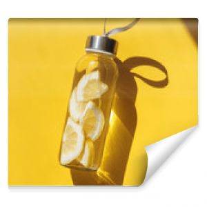 Glass bottle with lemon water drink detox at sunlight on yellow background. Healthy infused water boost metabolism and weight loss. Top view Aesthetic still life, refreshing summer drink