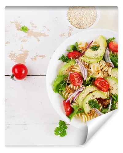 Fusilli pasta salad with avocado, tomatoes, fresh green lettuce, red onion and mustard dressing on white background. Vegetarian healthy lunch. Top view, flat lay