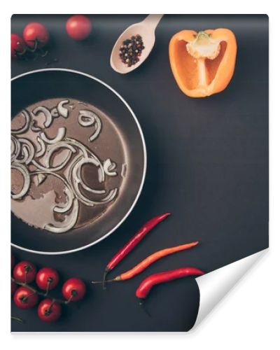 top view of frying pan with onion and oil among vegetables on gray table 