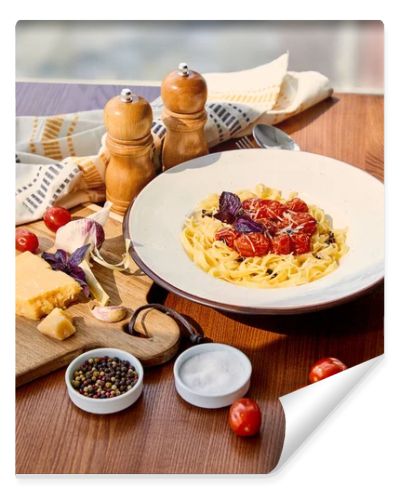 delicious pasta with tomatoes served on wooden table with napkin, seasoning and ingredients in sunlight