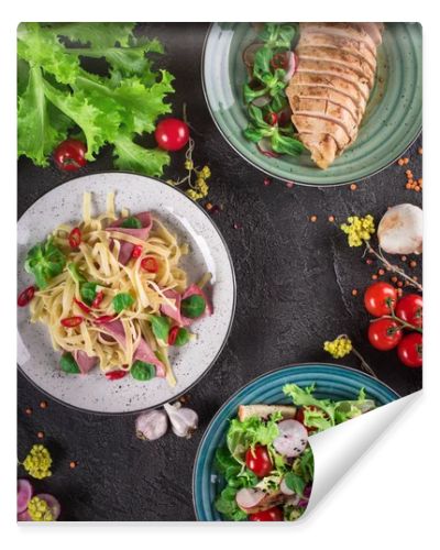 Delicious dinner. Italian pasta, fresh vegetable salad and roasted chicken breast on the black background. Healthy food. Close up. Top view