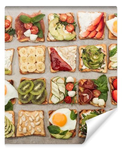 Top view of toasts with fried eggs, cut vegetables and fruits on textured surface