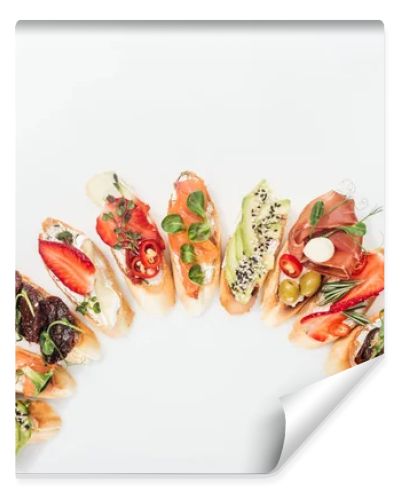 top view of delicious traditional italian bruschetta with prosciutto, salmon, fruits, vegetables and herbs on white