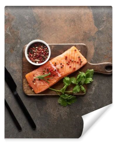 top view of raw fresh salmon with peppercorns, parsley on wooden cutting board near cutlery