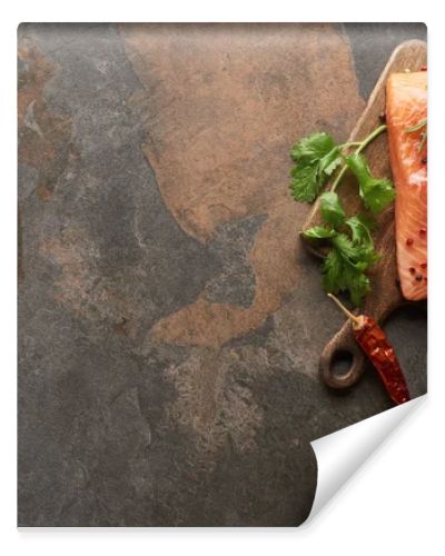 top view of raw fresh salmon with greenery, chili peppers and lemon on wooden cutting board