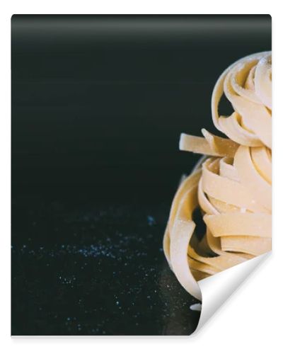 closeup view of raw tagliatelle pasta covered by flour on black background 