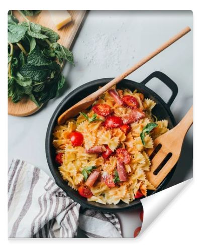 elevated view of pasta with jamon, cherry tomatoes, mint leaves covered by grated parmesan in pan with wooden spatula and spoon on marble table