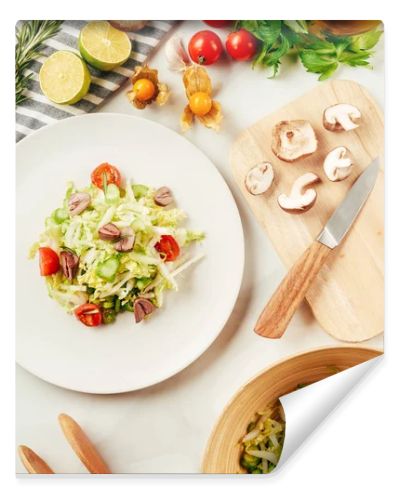 salad, cabbage and celery in plate with bottle of oil, cherry tomatoes, limes and mushrooms on cutting board 