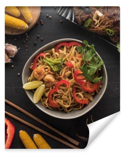 top view of tasty spicy seafood thai noodles near chopsticks and fresh ingredients on wooden grey surface