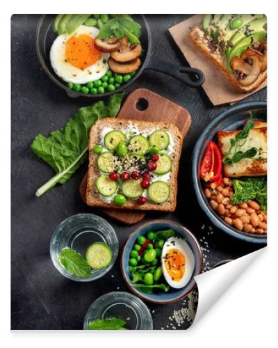 Tasty food with avocado toast, vegetables, eggs on dark background. Helthy breakfast concept. Top view, copy space.