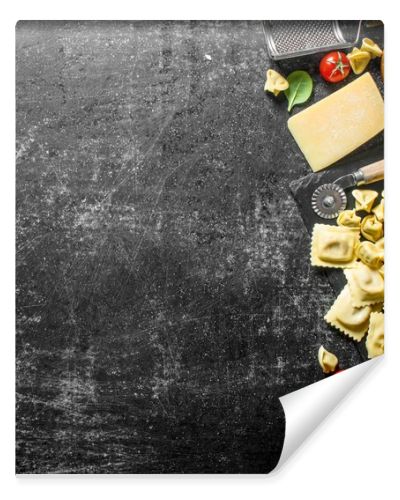 An assortment of different types of raw pasta with cheese, tomatoes and herbs. On dark rustic background