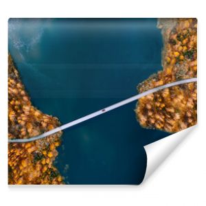 Aerial view of bridge road with red car over blue water lake or sea with island and autumn color woods in Finland.