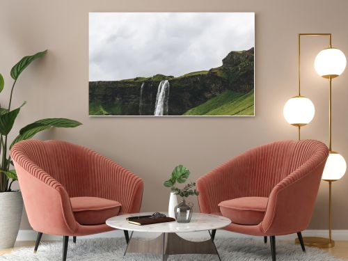scenic view of landscape with Seljalandsfoss waterfall in highlands under cloudy sky in Iceland 