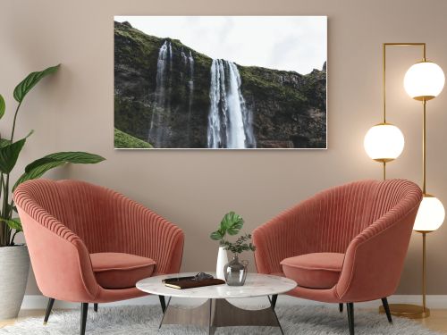 low angle view of Seljalandsfoss waterfall in highlands under cloudy sky in Iceland 