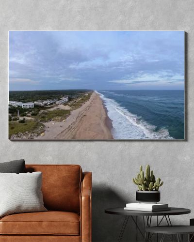 Drone panorama of Napeague on Long Islands South Fork, showing Atlantic Ocean surf, sandy beach, dunes and a beachfront resort complex at dusk.