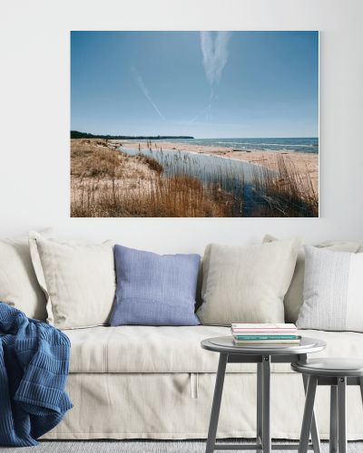 Scenic coastal landscape with sandy beach, calm lagoon and tall reeds under a bright blue sky crossed by airplane contrails. Natural shoreline with copy space, ideal for travel, environment and tourism concepts.