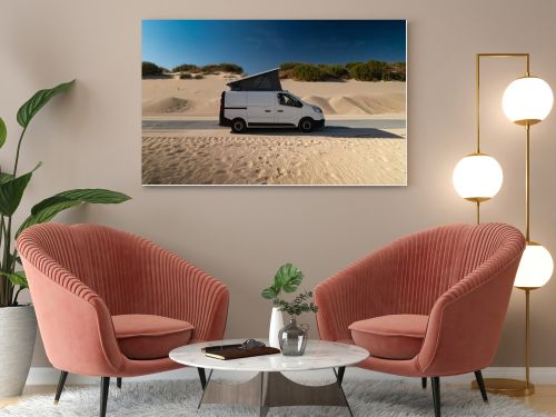 White camper van with pop top roof parked near sand dunes along the coast of Tarifa, Cadiz, Spain. Concept of vanlife, road trip adventure, freedom, and camping mobility.